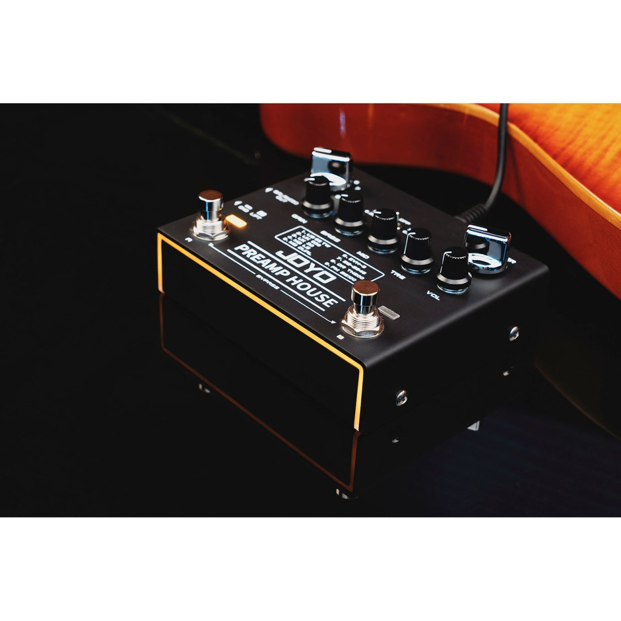 Düğmeler ve anahtarlar içeren siyah bir JOYO Preamp House gitar pedalı, bir gitarın yanında.