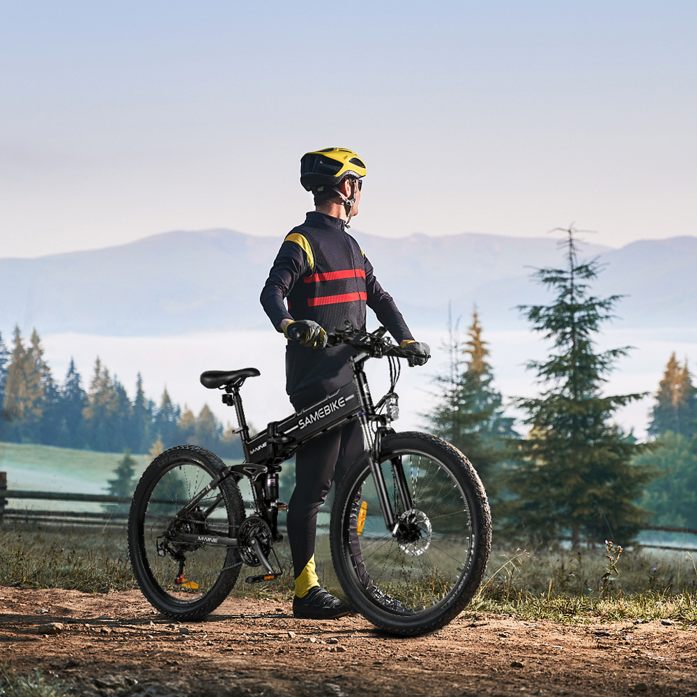 Hombre con casco junto a bicicleta plegable negra en paisaje montañoso.