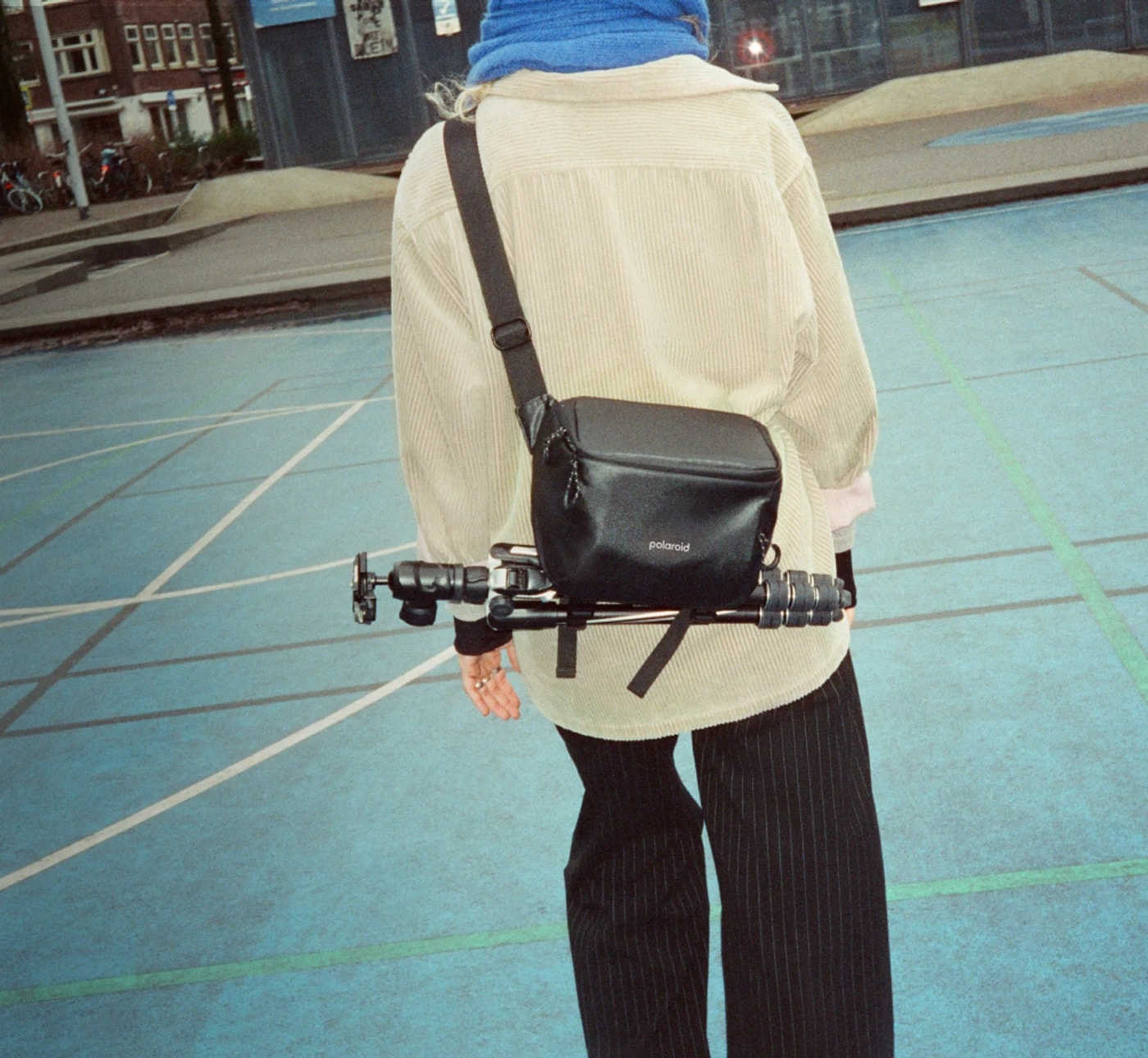 Person im Cordjackett und gestreifter Hose trägt Kamerarig und Polaroid-Tasche.