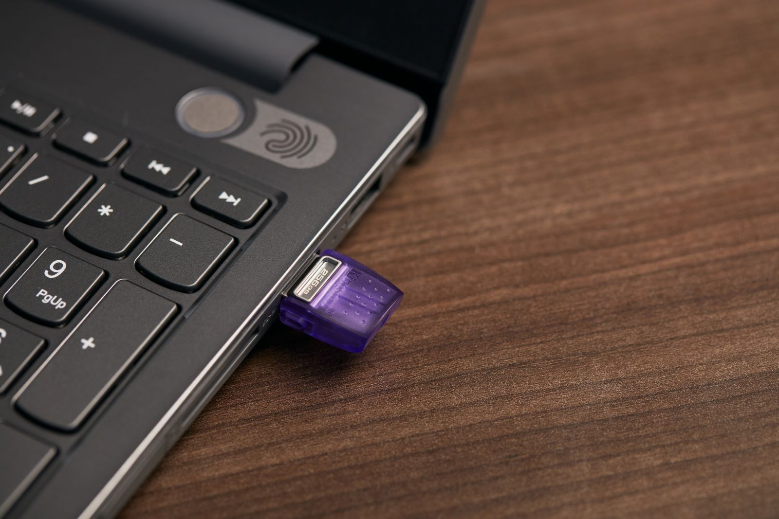 Een paarse USB-stick is aangesloten op een laptop op een houten oppervlak.