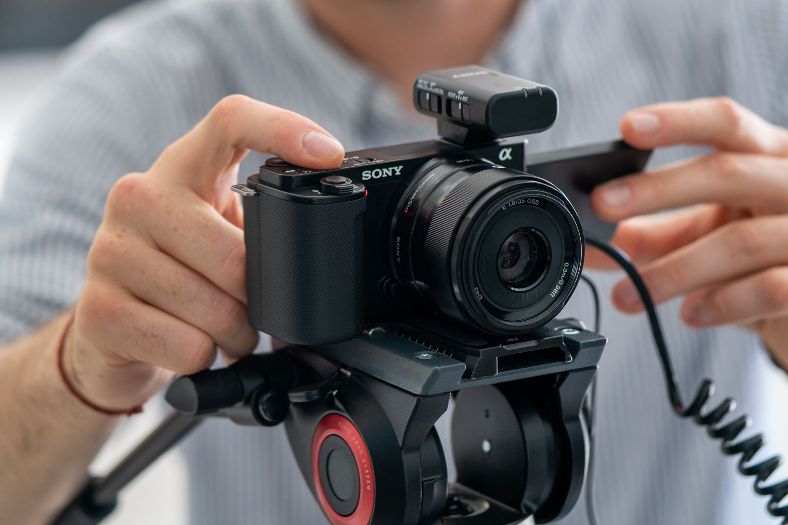 Osoba ustawia czarny aparat Sony z mikrofonem na statywie.