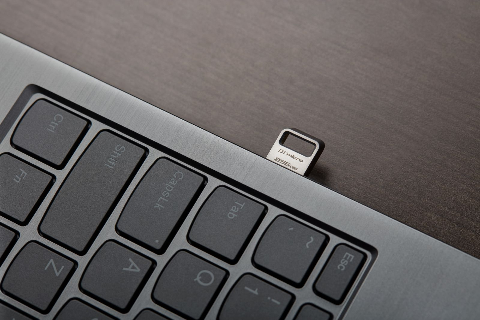 Srebrny pendrive 256 GB jest podłączony do klawiatury laptopa.