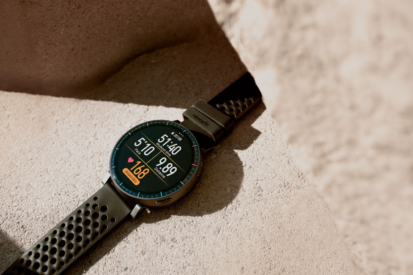 Eine grüne Sportuhr mit Trainingsdaten auf dem Display liegt auf hellem Sand.