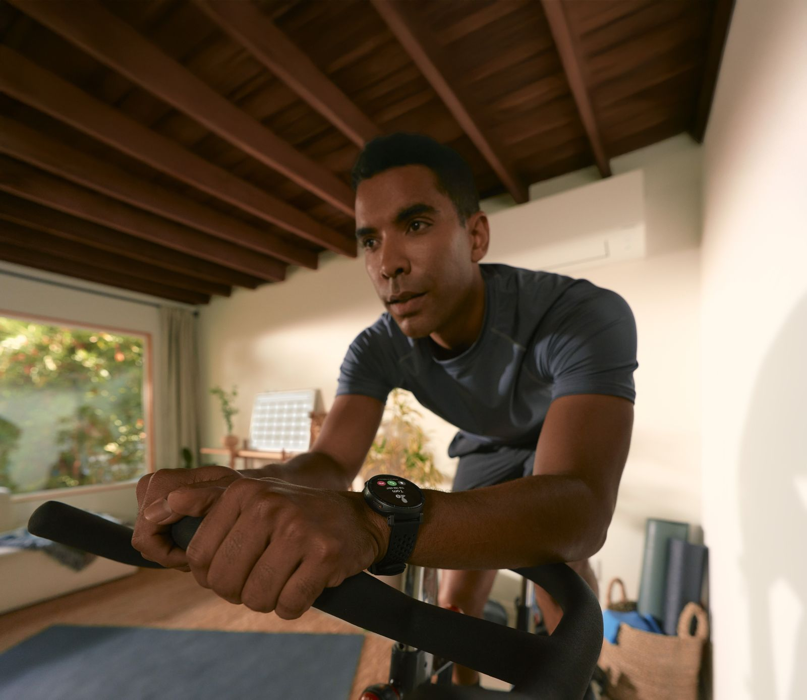 Mann auf Heimtrainer, trägt eine Smartwatch, trainiert im Raum.