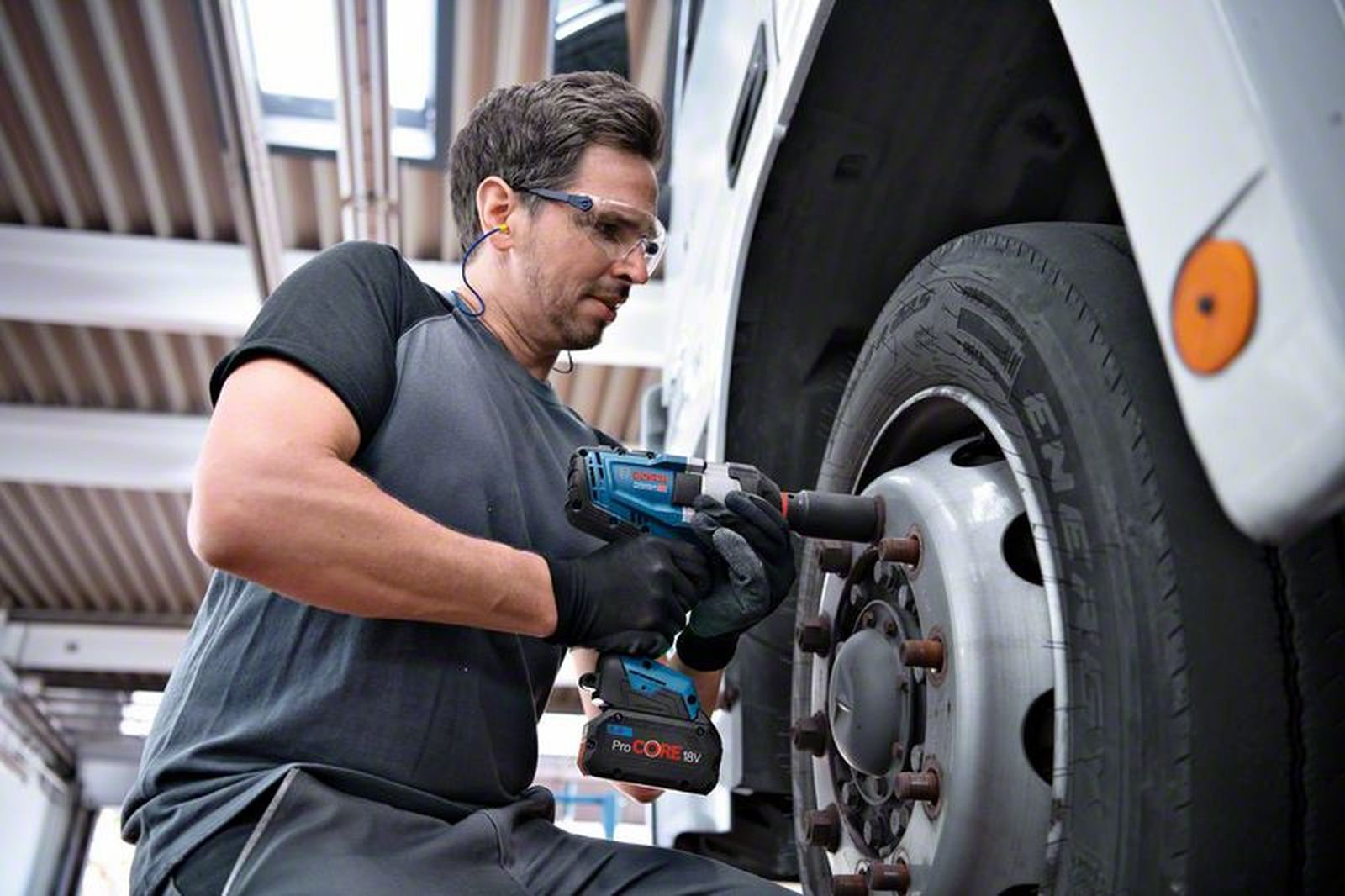 Mann mit Schutzbrille benutzt Schlagschrauber an LKW-Rad.