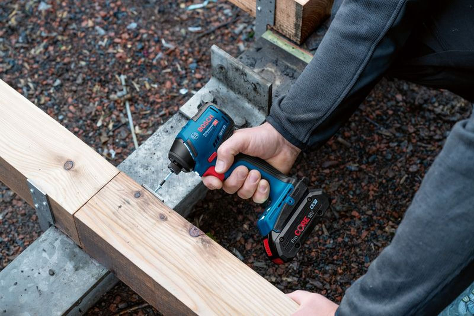 Ein Mann benutzt einen blauen Bosch Akkuschrauber, um eine Schraube in Holz zu drehen.