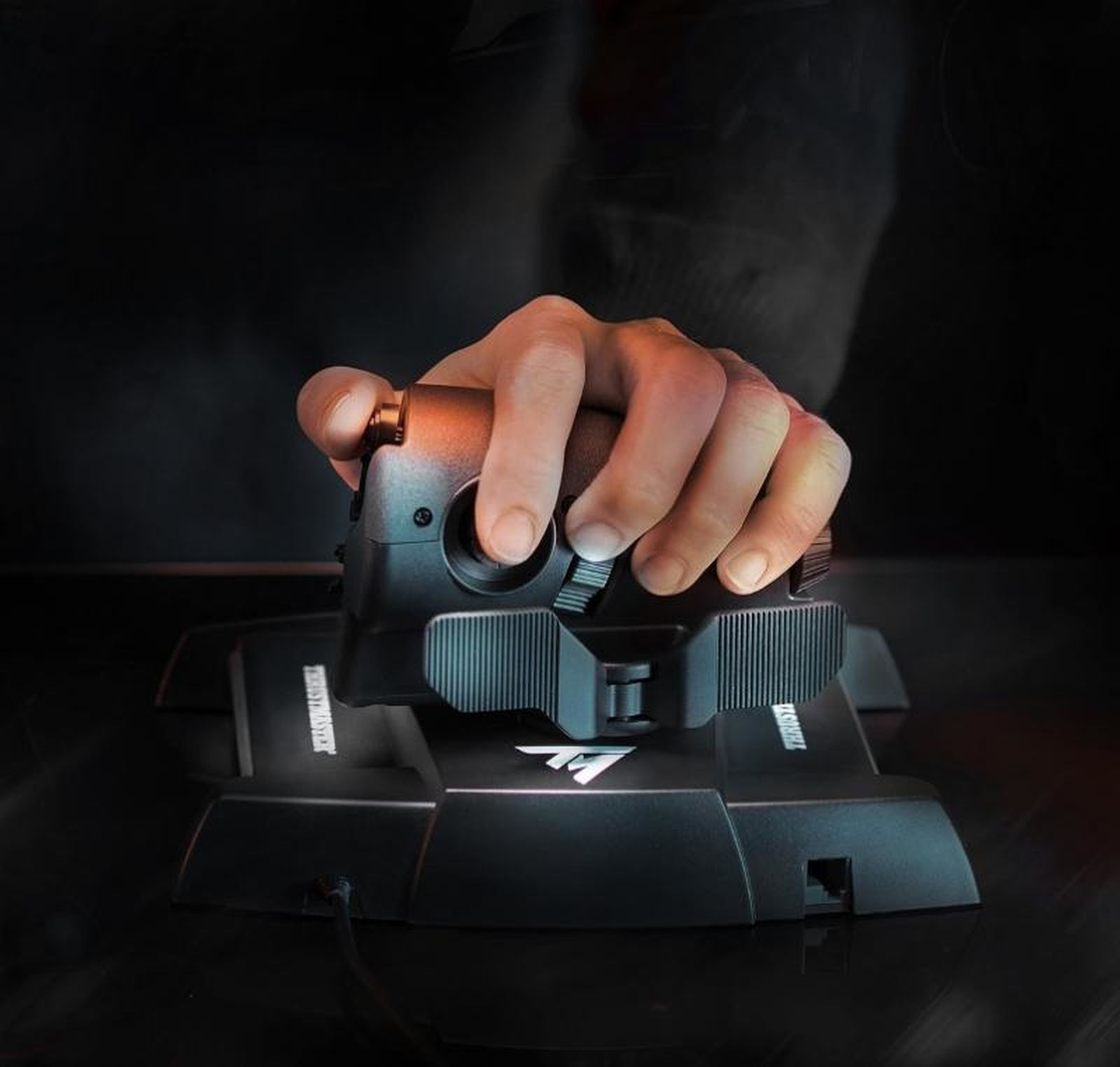 Une main agrippe un joystick noir avec une base texturée sur fond sombre.