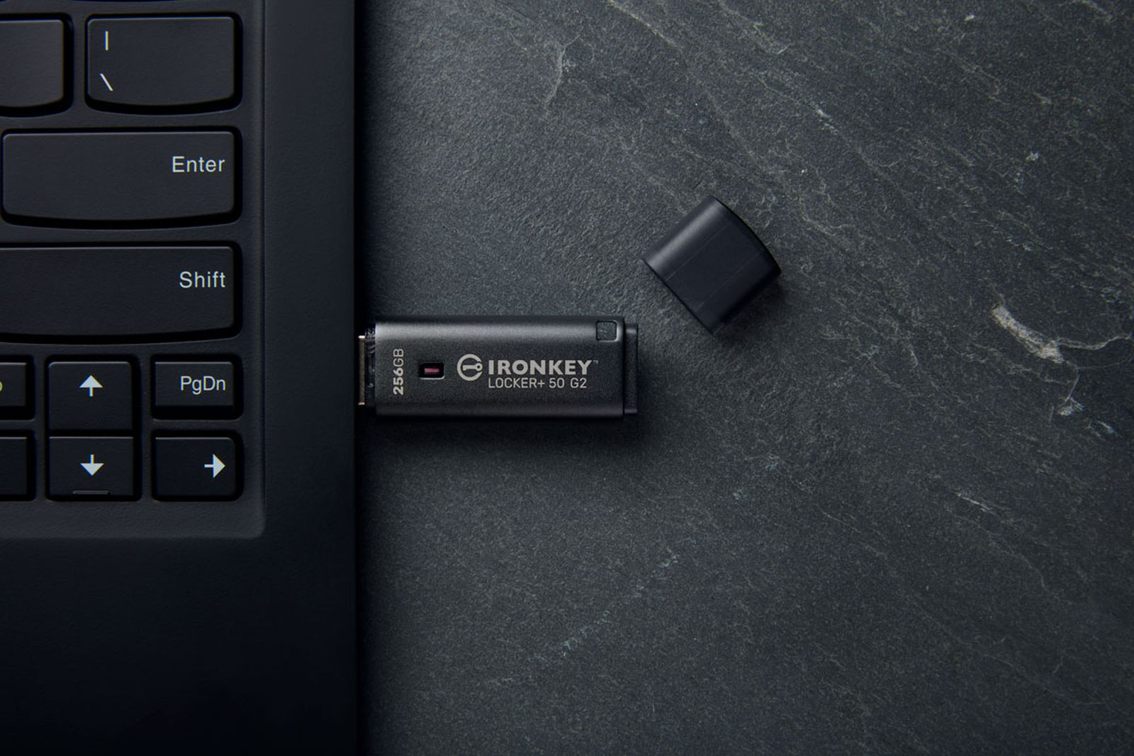 Un'unità USB Ironkey nera è inserita nella tastiera di un laptop. Il suo tappo è accanto.