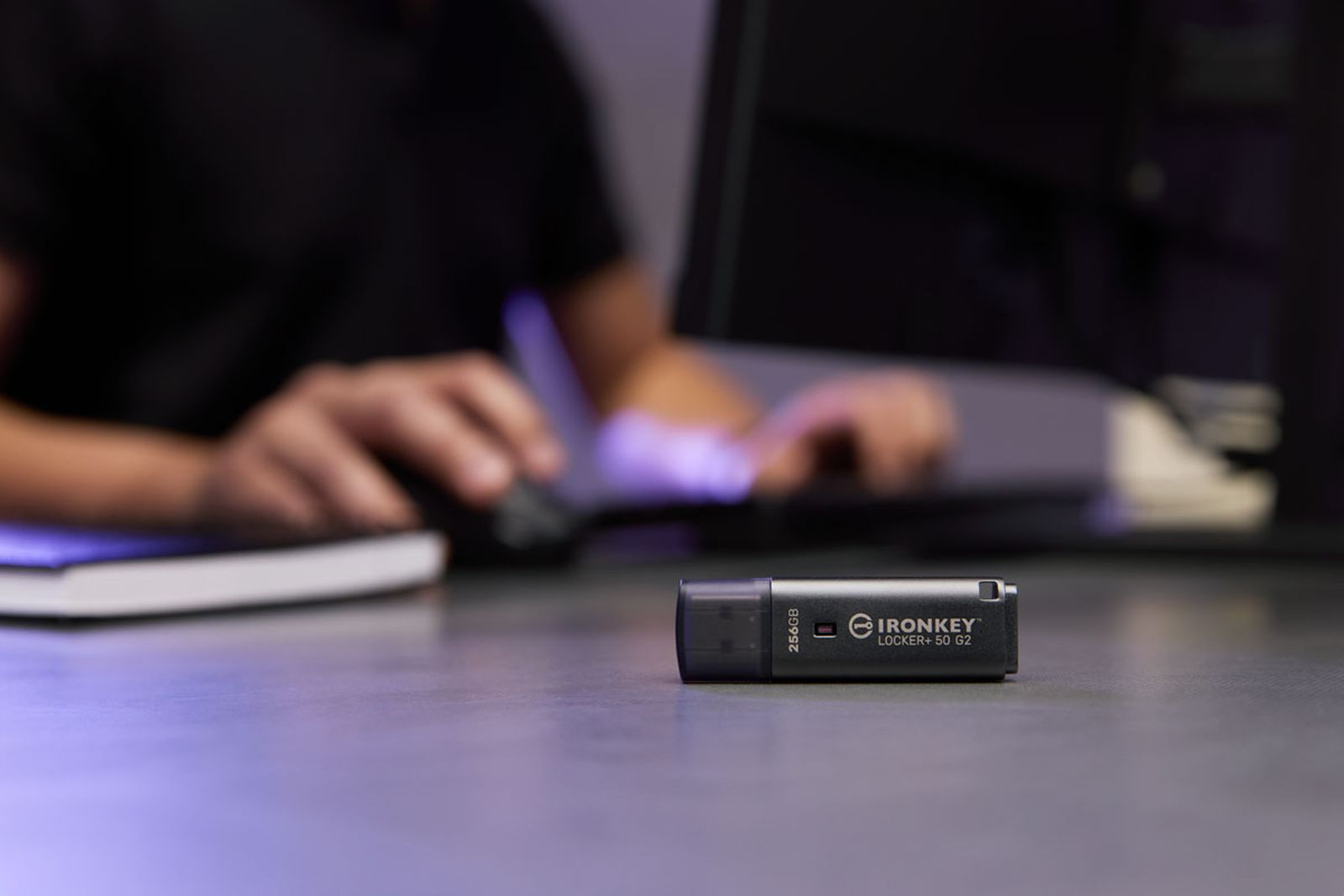 Un'unità USB è su una scrivania, una persona usa un mouse sullo sfondo.