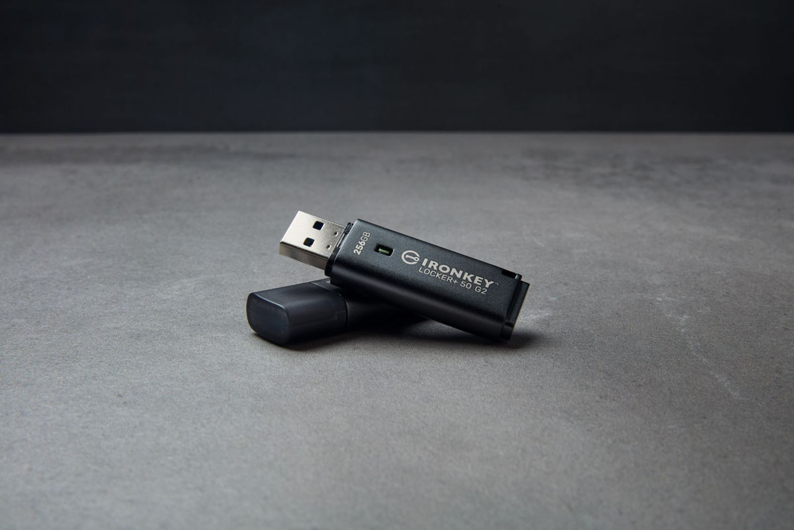 Un'unità flash USB nera con il suo tappo giace su una superficie grigia.