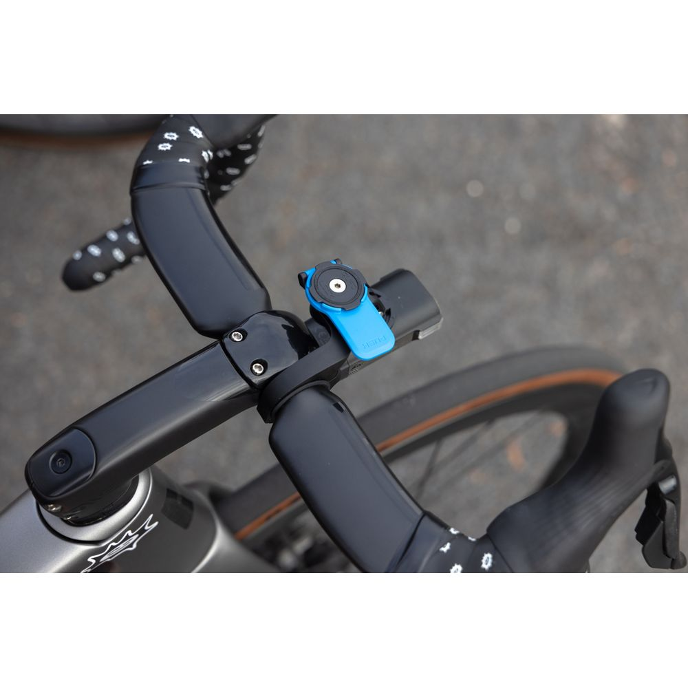 Blauer Fahrradhalter am Lenker mit schwarzem Vorbau und Reifen im Hintergrund.