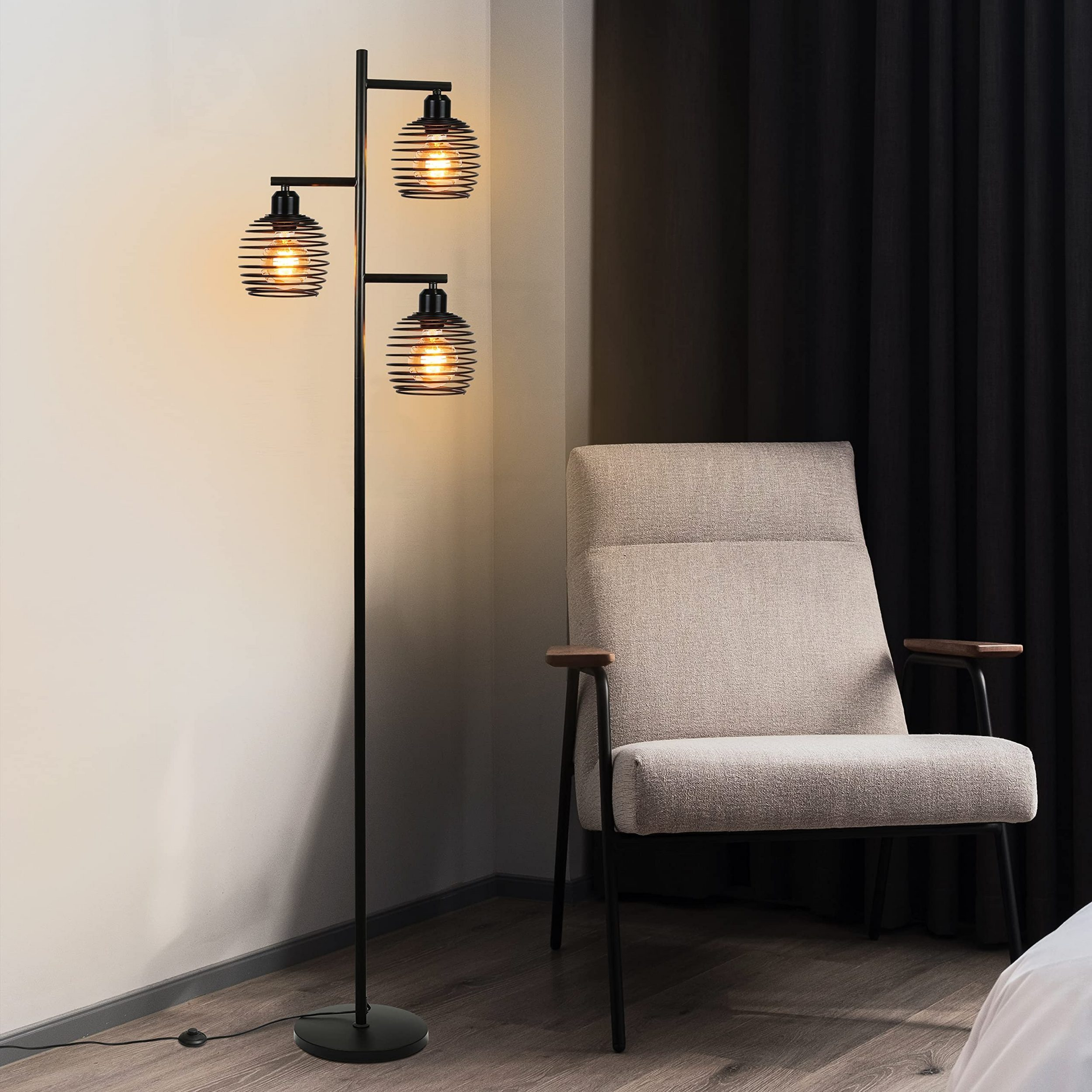 Lampada da terra a tre teste con paralumi a gabbia in metallo nero accanto a una poltrona color crema.