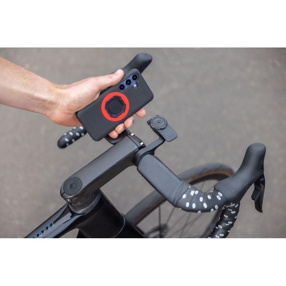 Hand hält Smartphone mit rotem Ringhalter über Fahrradlenker.