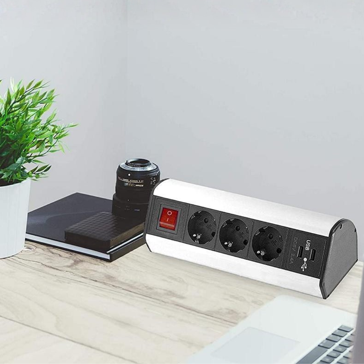 Eine weiße Steckdosenleiste mit drei Steckplätzen und zwei USB-Anschlüssen auf einem Holztisch.