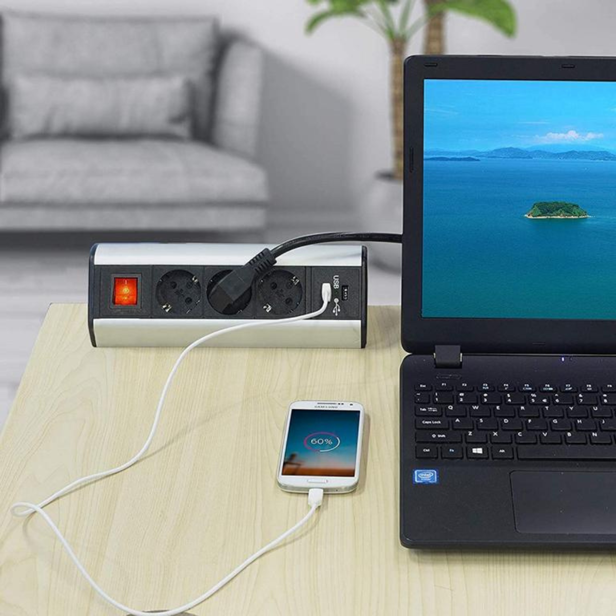 Ein Laptop und ein Handy laden über eine Steckdosenleiste auf einem Holztisch.