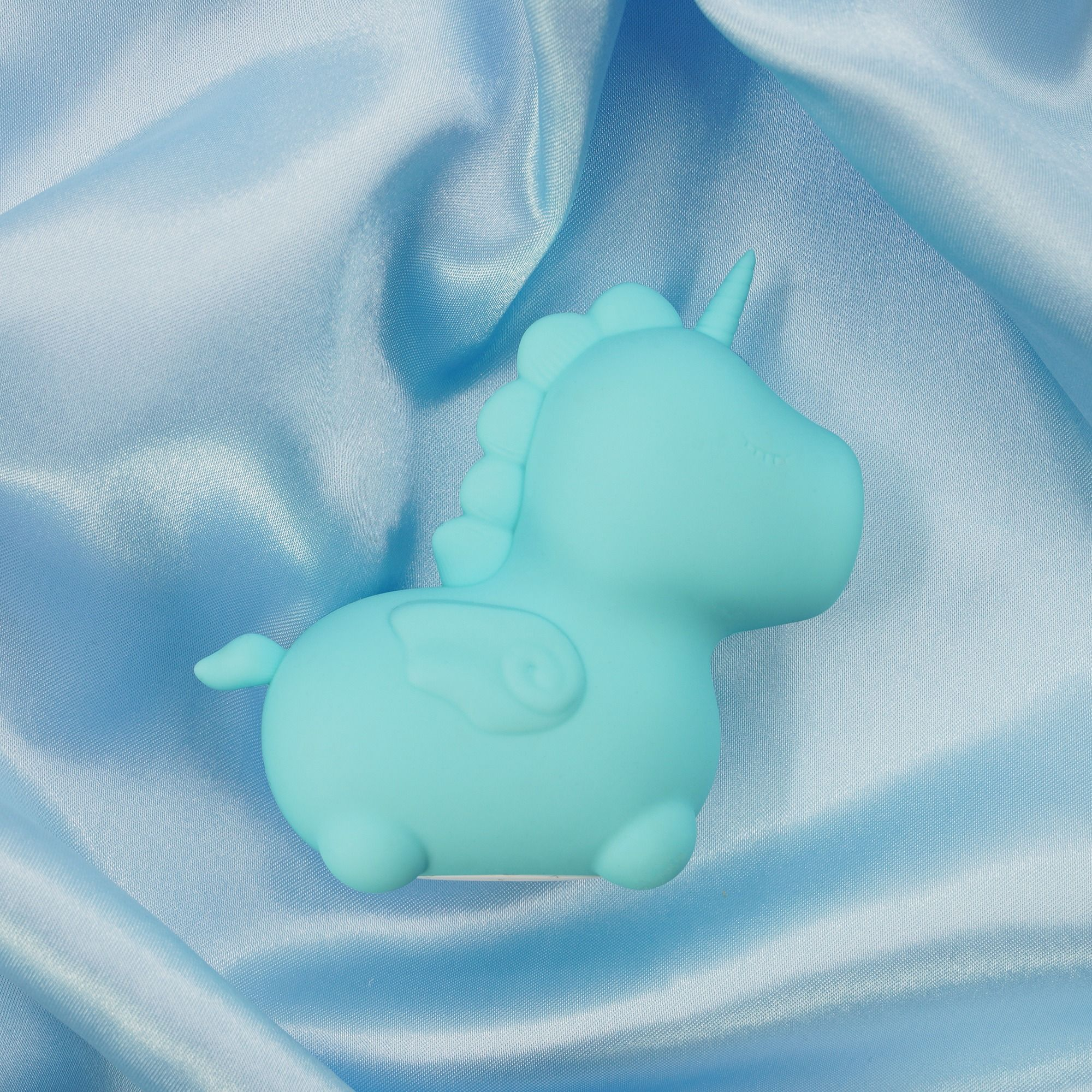 Ein türkisfarbener Einhorn-Radiergummi auf blauem Satin.