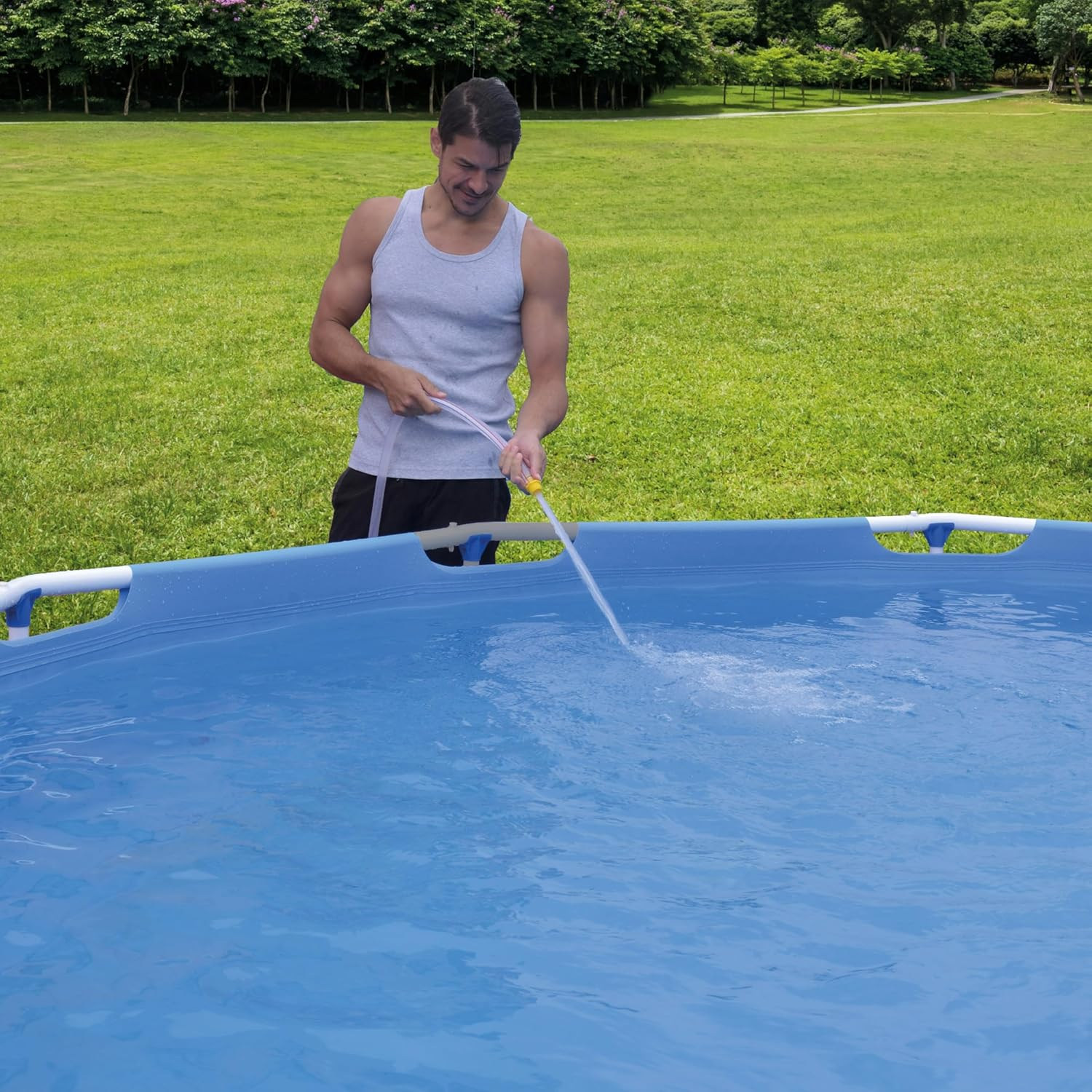 Ein Mann füllt einen blauen Pool mit einem Schlauch in einem grünen Garten.