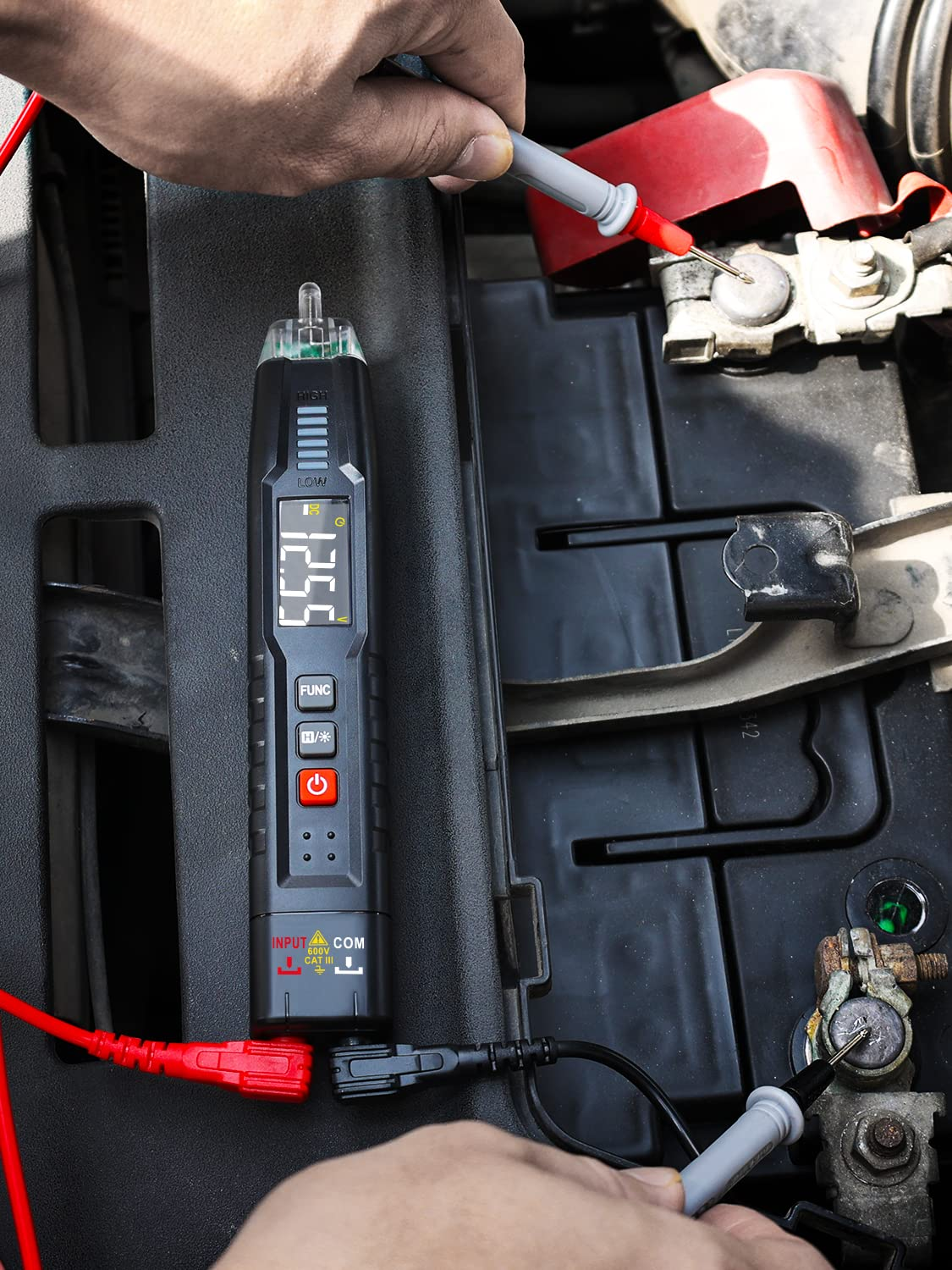 Eine Hand benutzt ein digitales Multimeter an einer Autobatterie, um die Spannung zu messen.