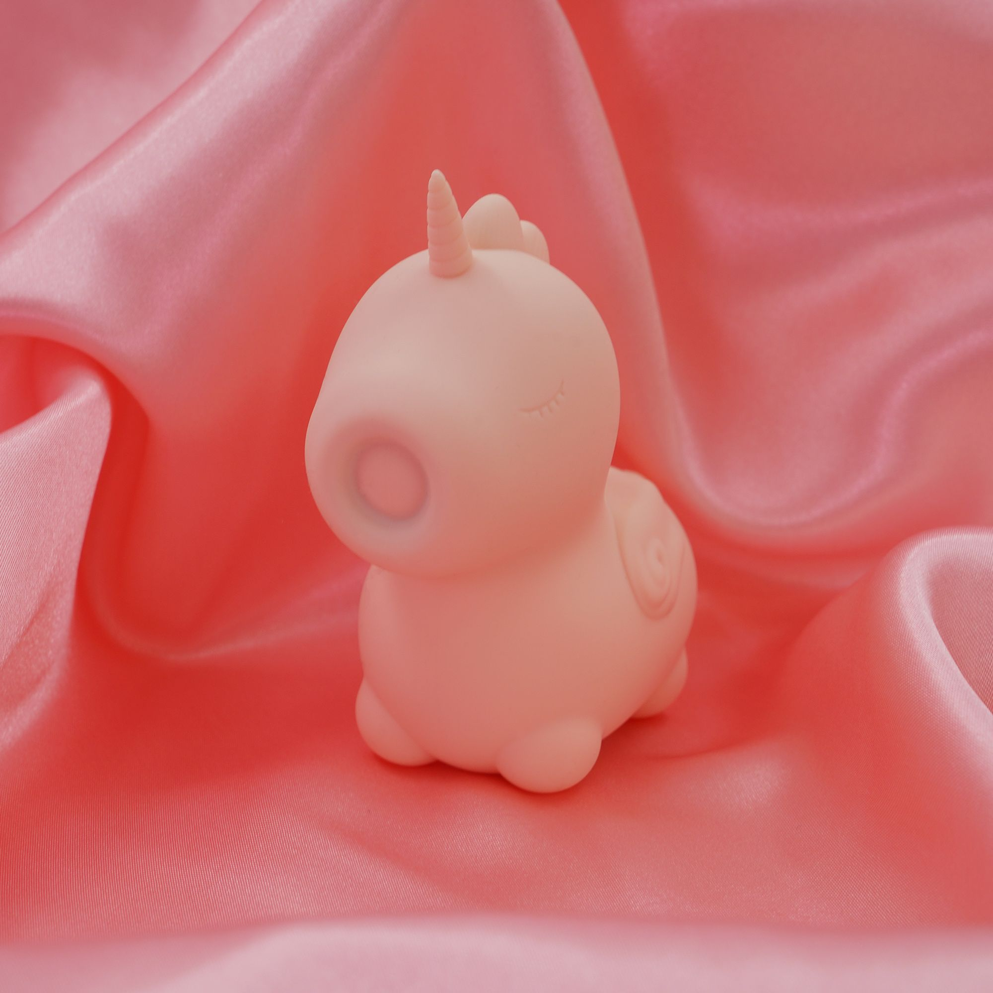 Ein kleines rosa Einhorn-Spielzeug liegt auf glänzendem rosa Stoff.