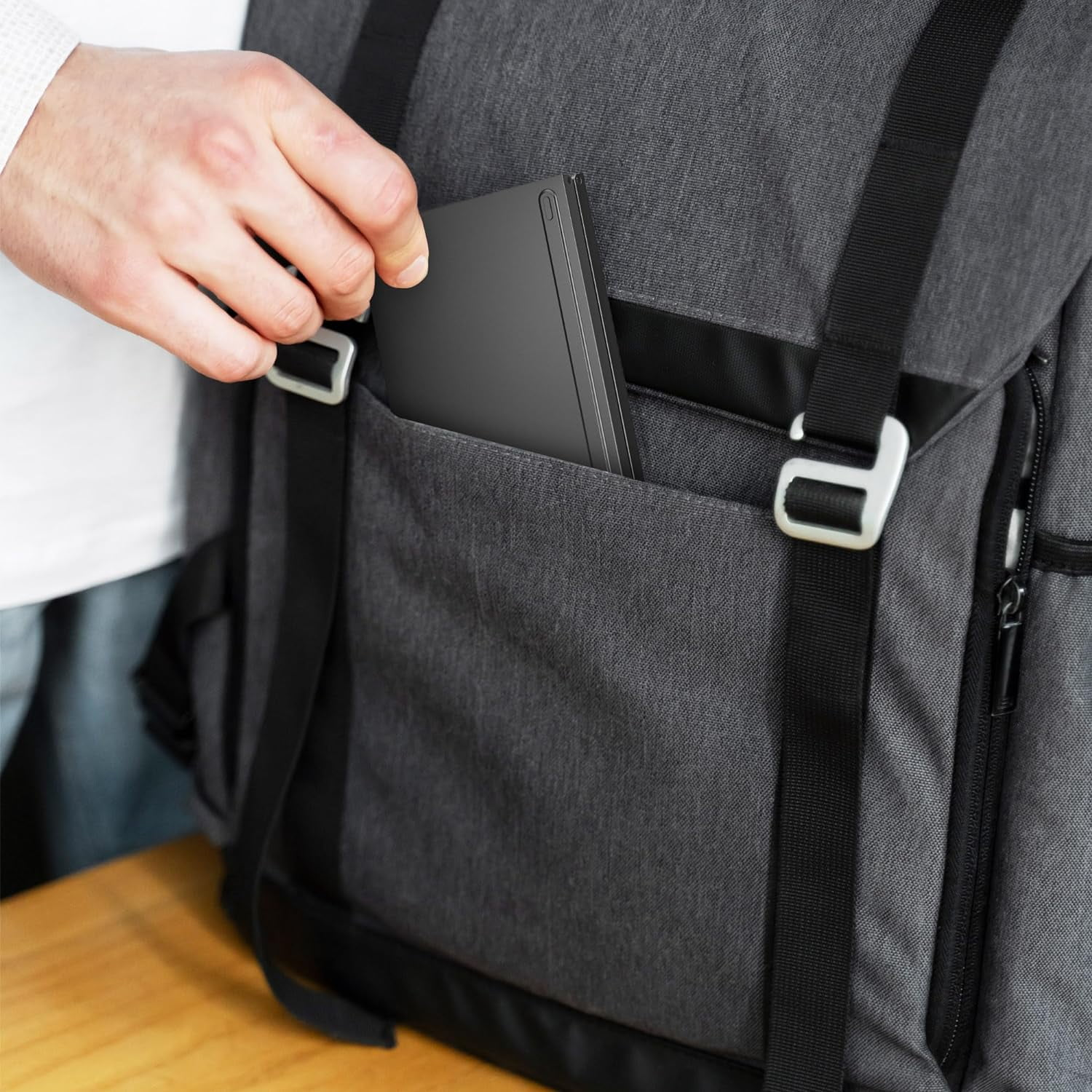 Eine Hand legt ein dunkles, schmales graues Gerät in eine dunkle graue Rucksacktasche.
