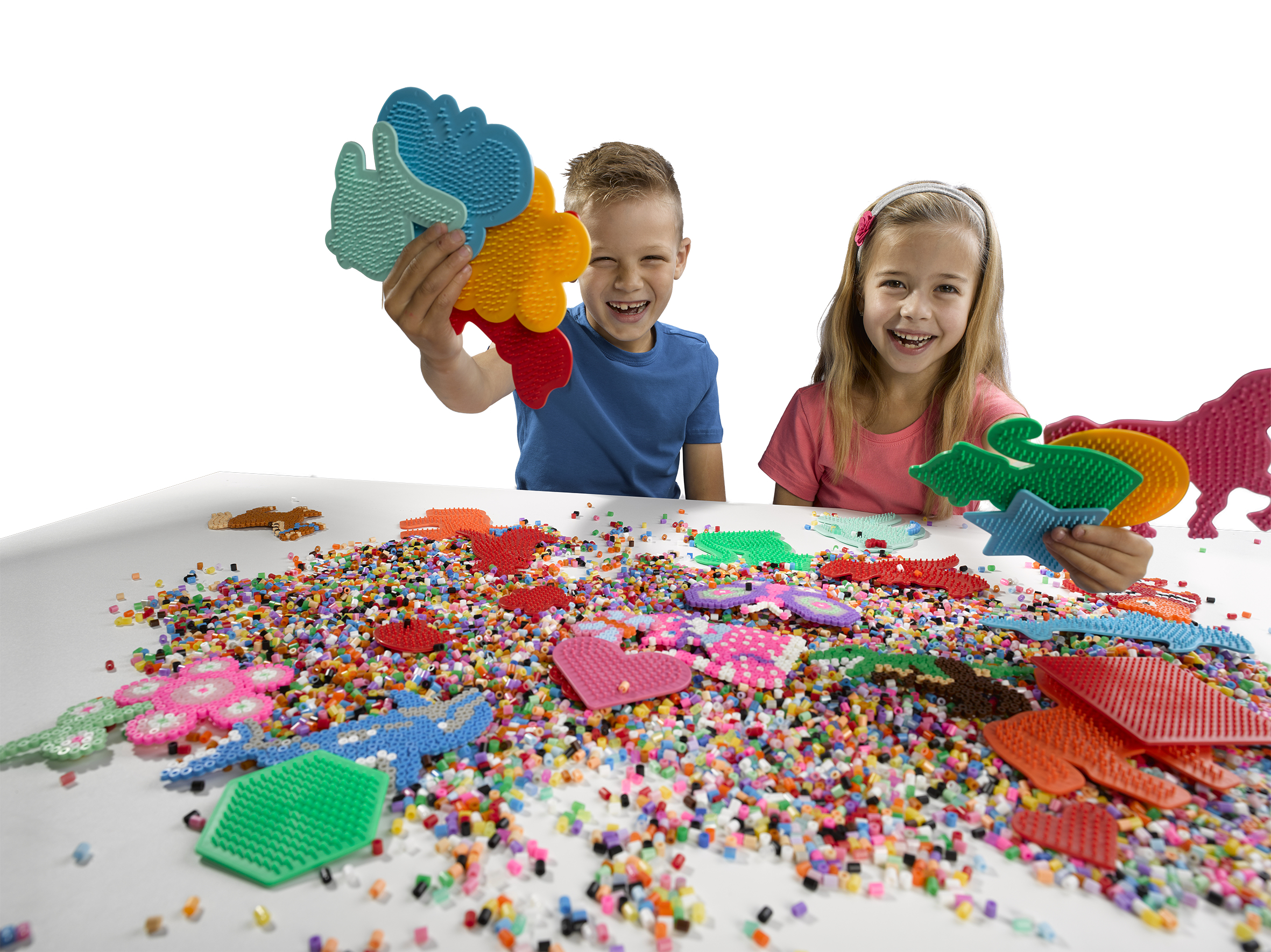 Zwei lachende Kinder sitzen an einem Tisch voller bunter Perlen und Formen.