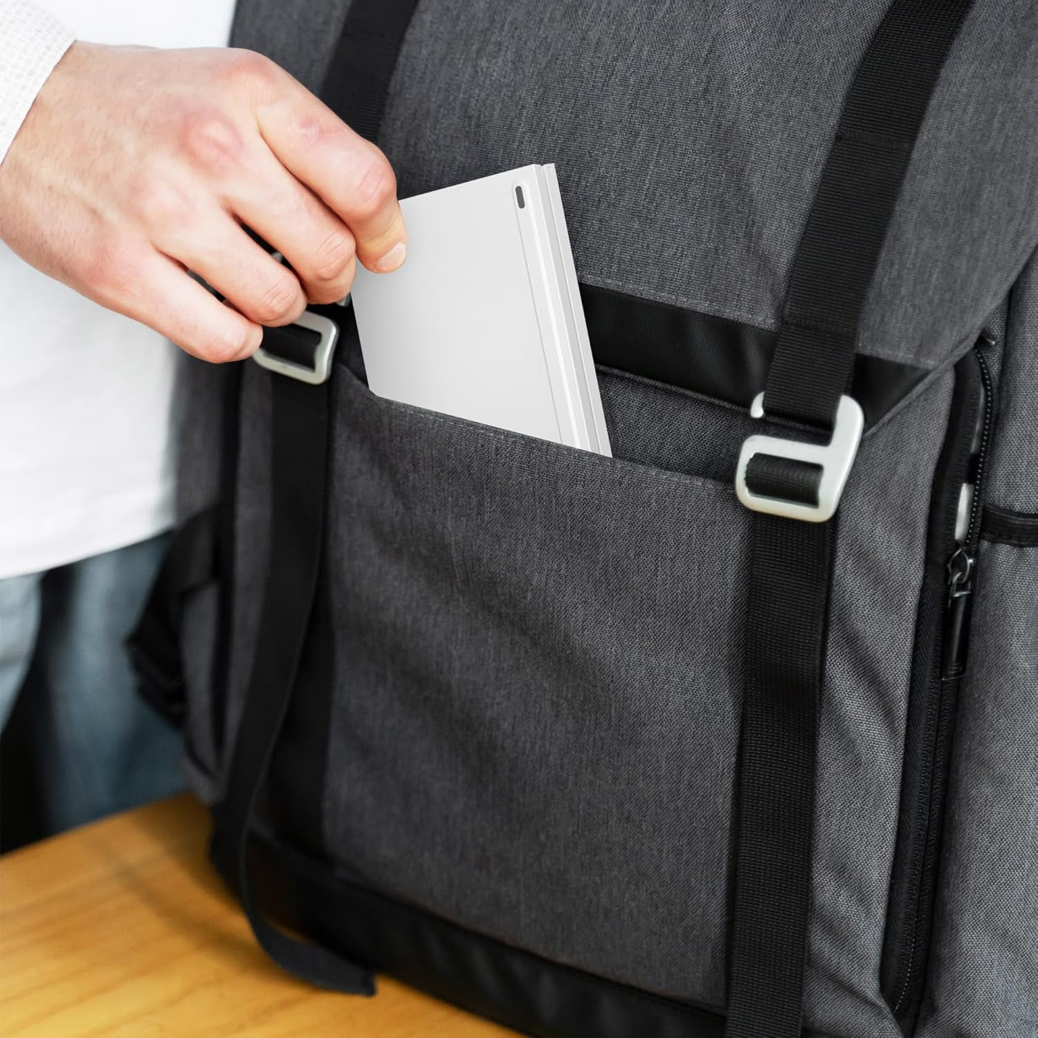 Eine Hand steckt ein dünnes silbernes Gerät in eine graue Rucksacktasche.