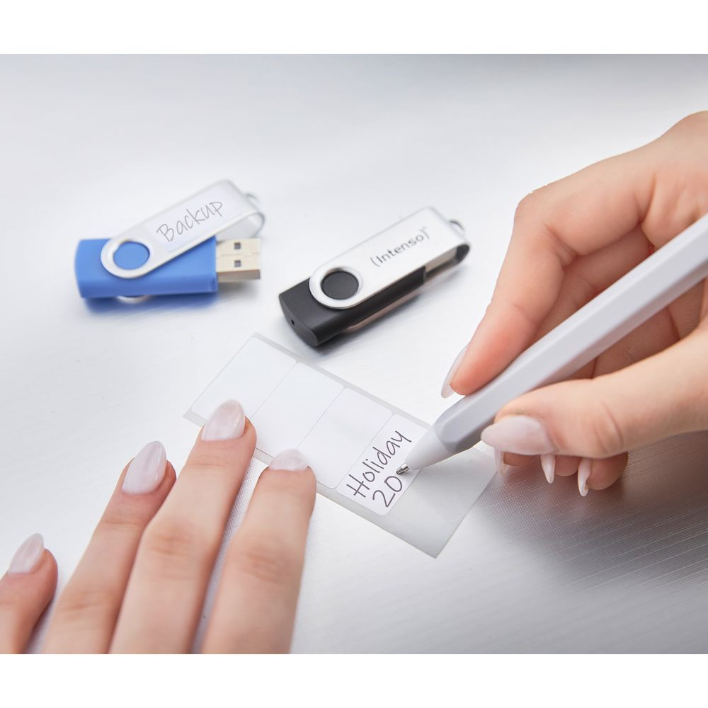 Person beschriftet Aufkleber mit Stift, neben zwei USB-Sticks.