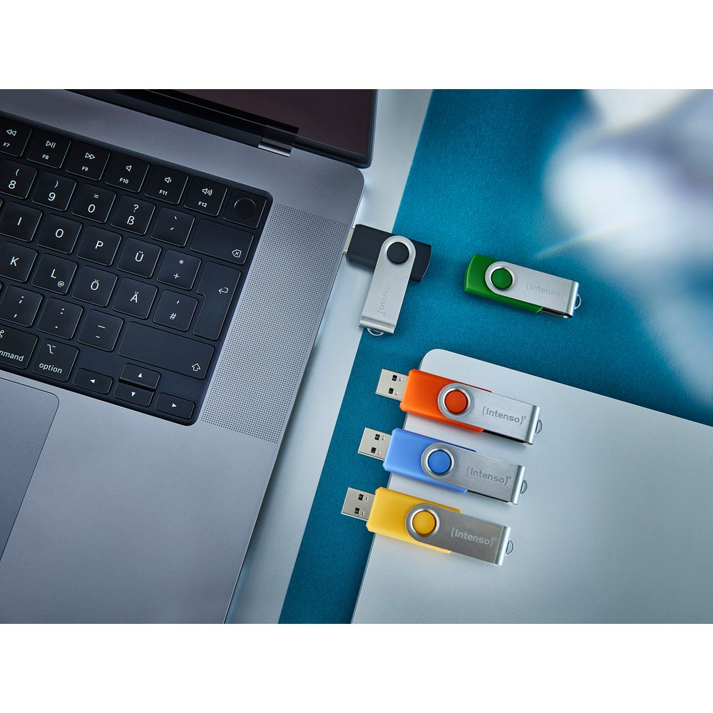 Ein Laptop mit mehreren bunten USB-Sticks daneben auf einer blauen und grauen Oberfläche.