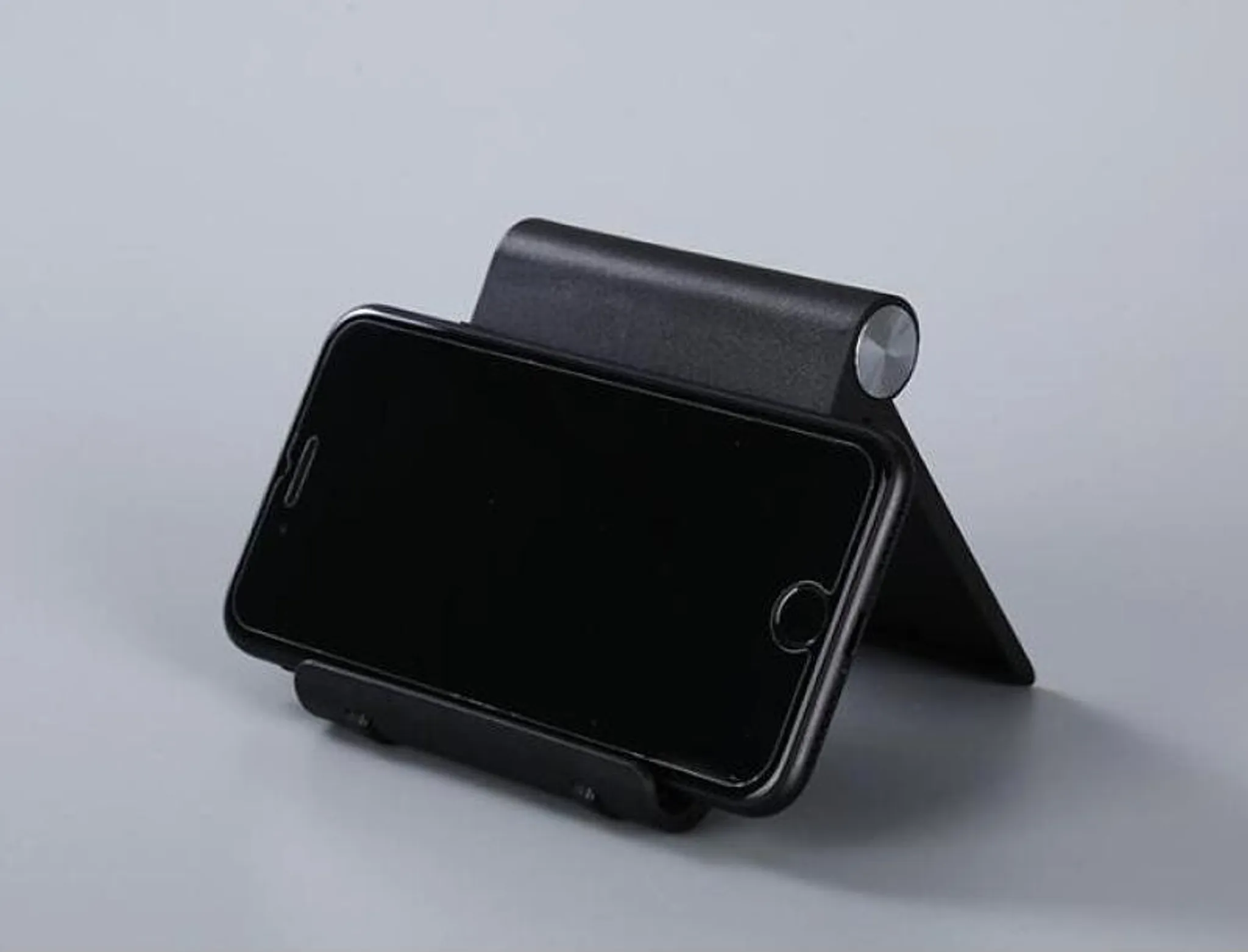 Ein schwarzer Handyhalter mit einem Smartphone, auf grauem Hintergrund.