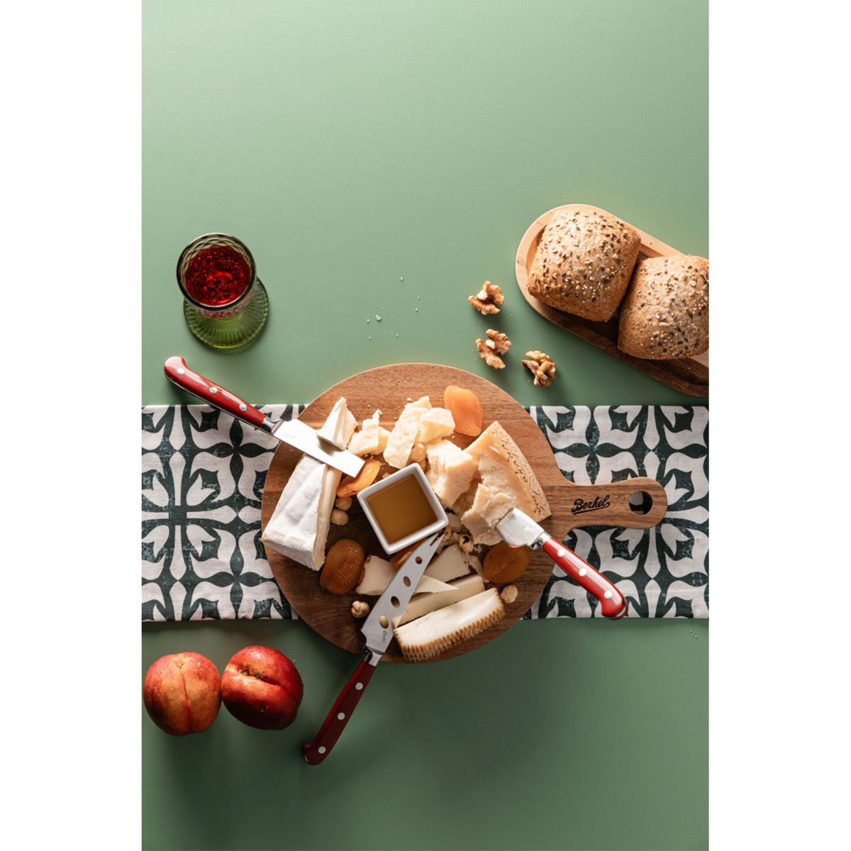 Käseplatte mit Brot, Nüssen, Früchten, Honig und Wein auf grünem Hintergrund.
