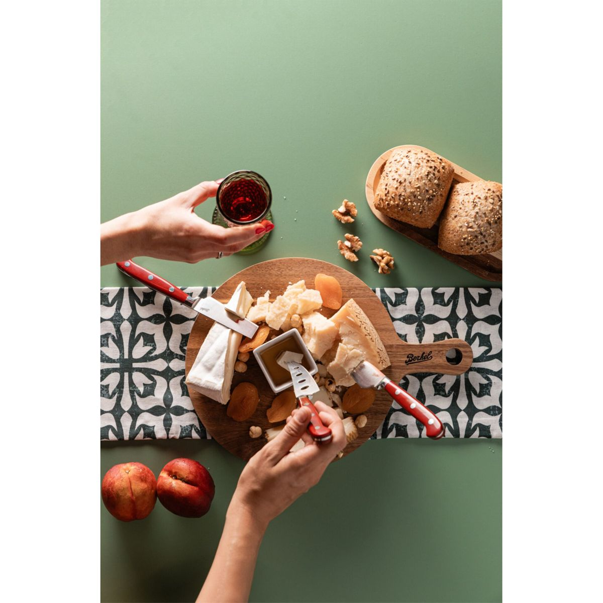 Käseplatte mit Brot, Nüssen, Obst und Rotwein auf grünem Hintergrund.