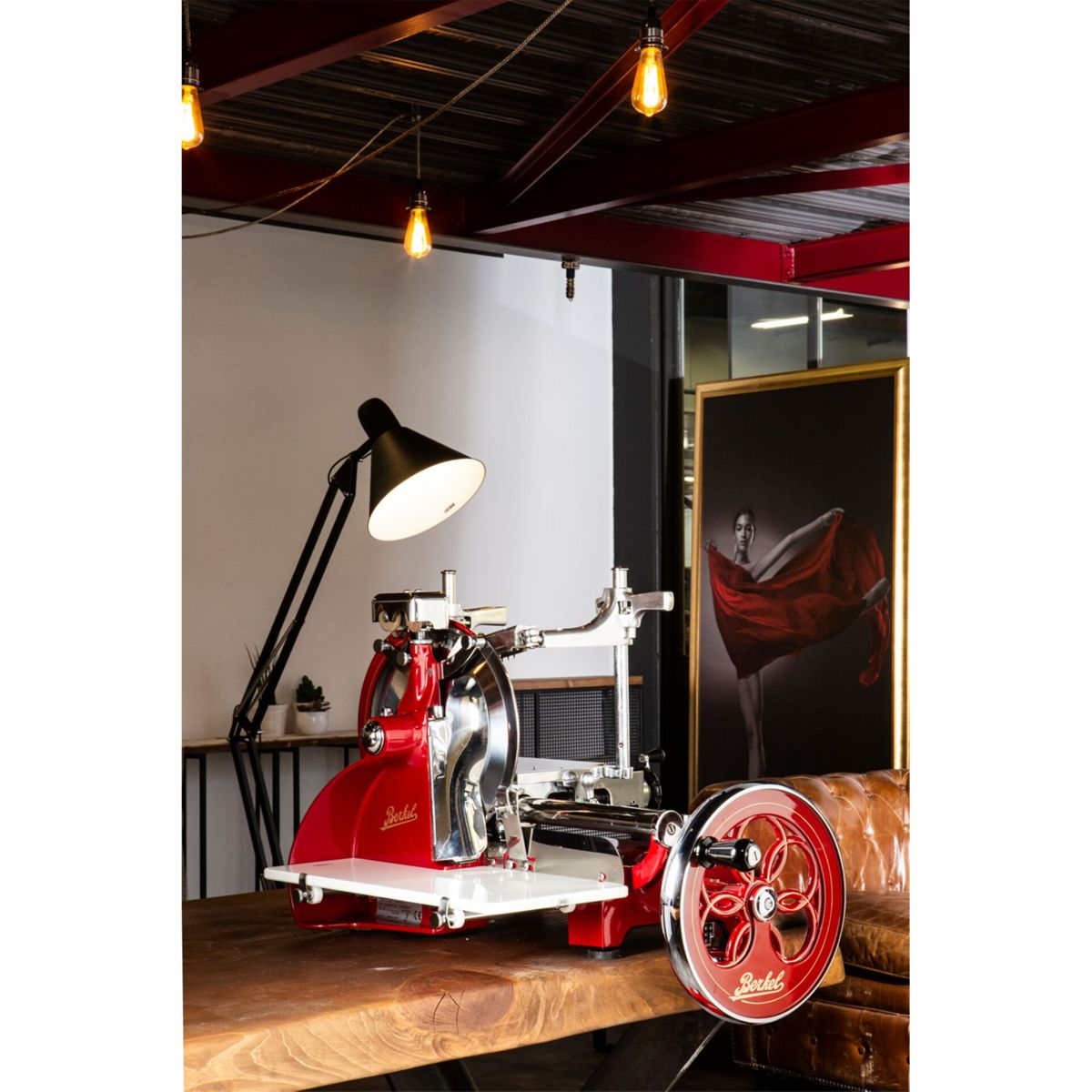 Affettatrice Berkel rossa su tavolo di legno, con lampada e opera d'arte sullo sfondo.