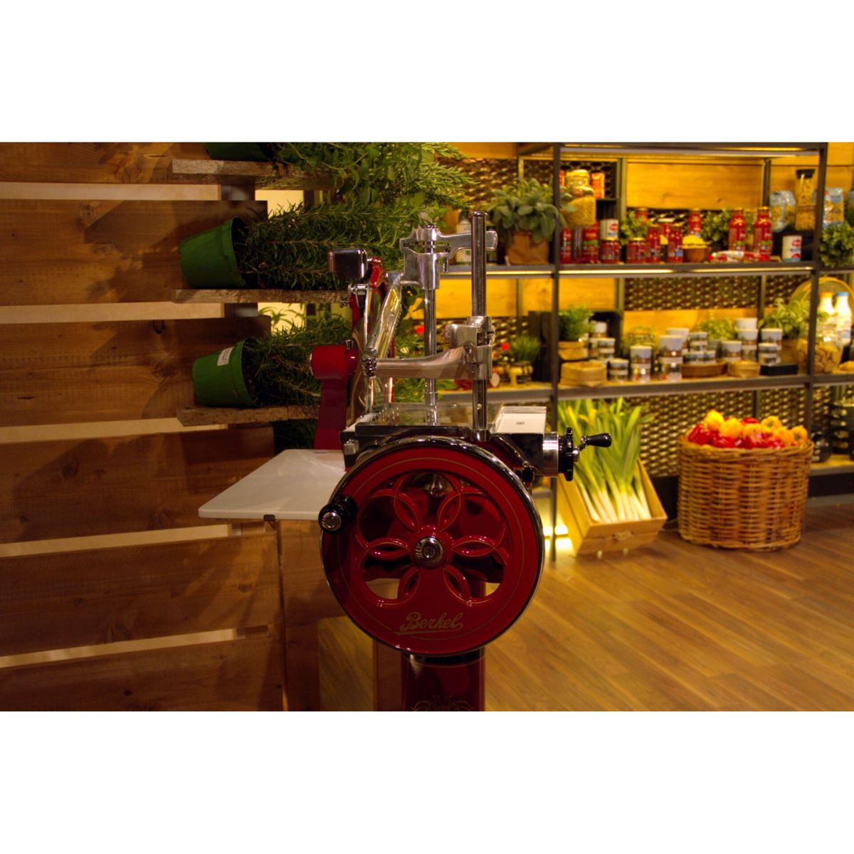 Affettatrice Berkel rossa con ruota in metallo in un negozio con scaffali pieni di cibo.