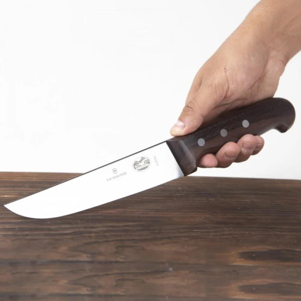 Bir el, ahşap masa üzerinde koyu ahşap saplı Victorinox bıçağı tutuyor.