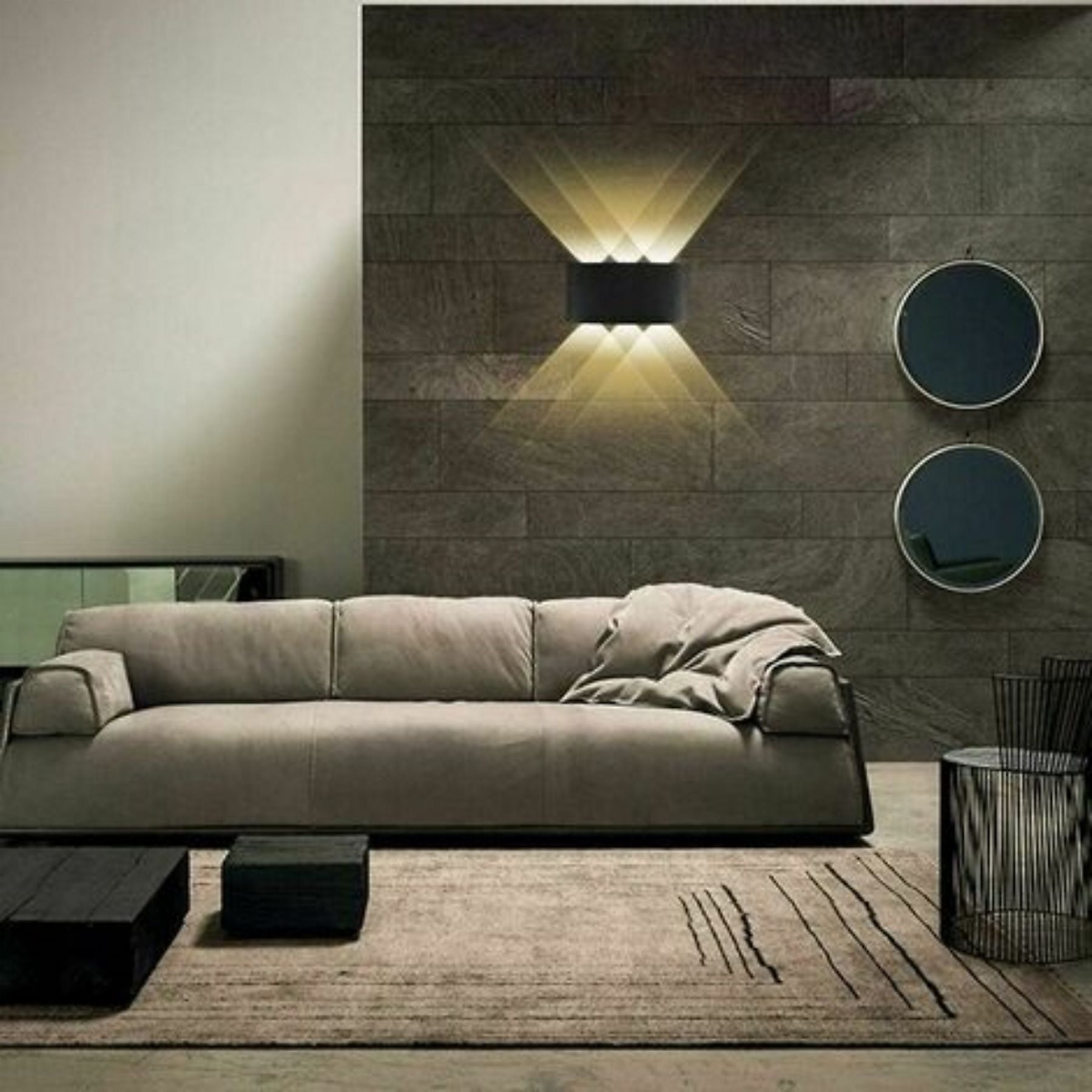 Ein modernes Wohnzimmer mit einem hellbraunen Sofa, schwarzen Couchtischen und einer gemusterten Wand mit Leuchte.