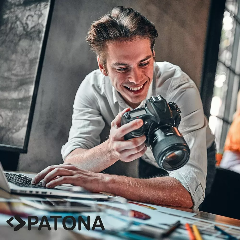 Un uomo in camicia bianca tiene una fotocamera e digita su un laptop.