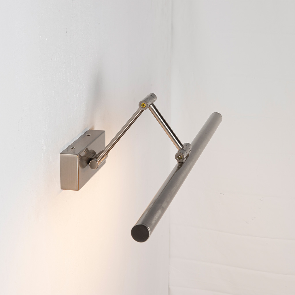 Una lámpara de escritorio plateada con brazo articulado cuelga de una pared blanca.