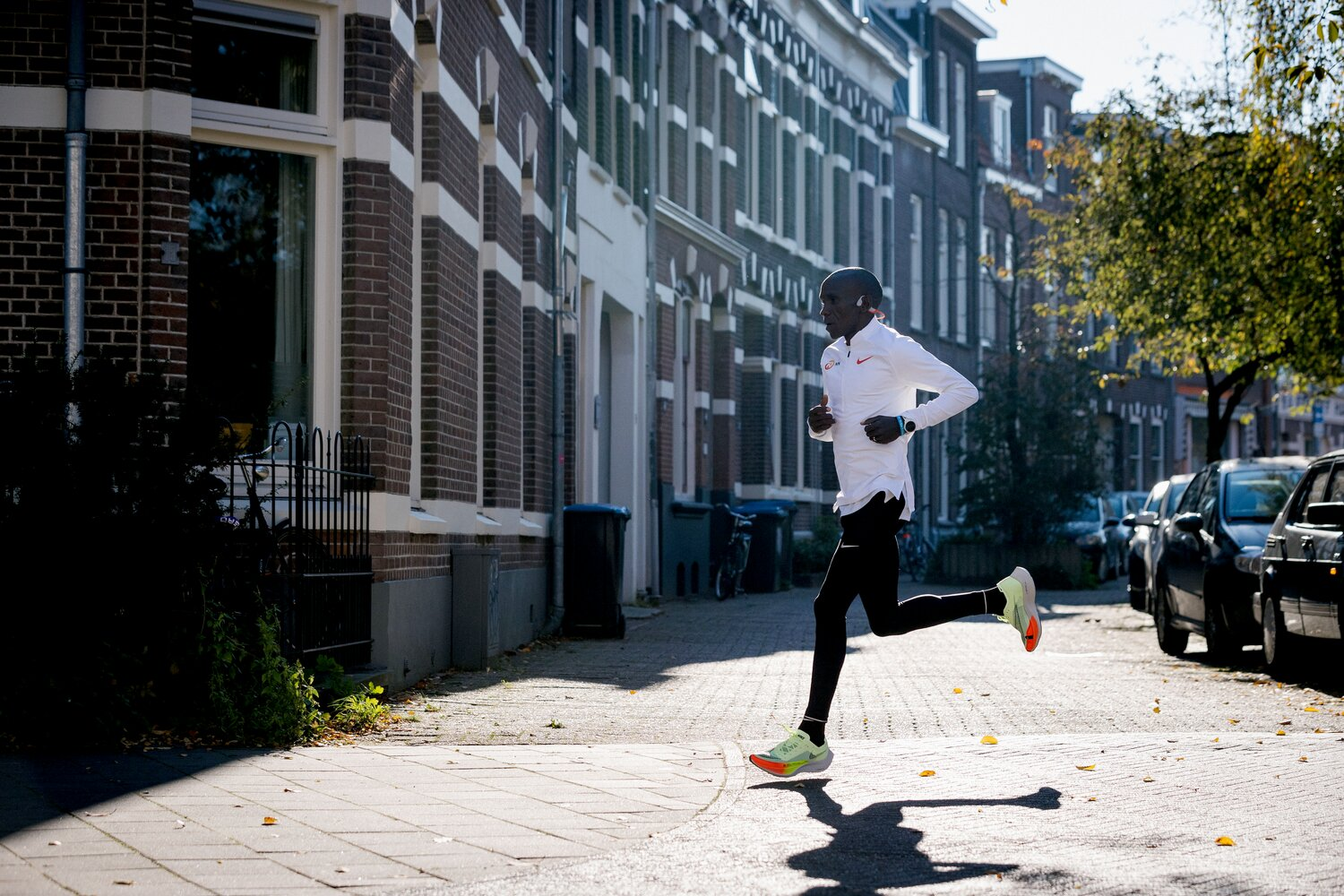 Mężczyzna w białej bluzce z długim rękawem i czarnych spodniach biegnie chodnikiem.