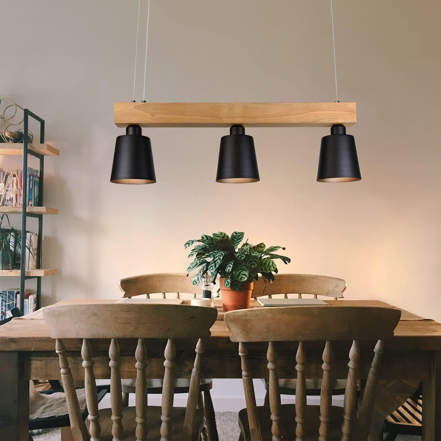 Drei schwarze Pendelleuchten hängen über einem Holztisch mit Stühlen. Eine Pflanze steht auf dem Tisch.
