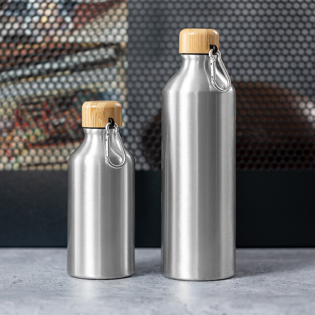 Dos botellas de agua de metal plateado con tapas de bambú y clips de mosquetón sobre una superficie gris.