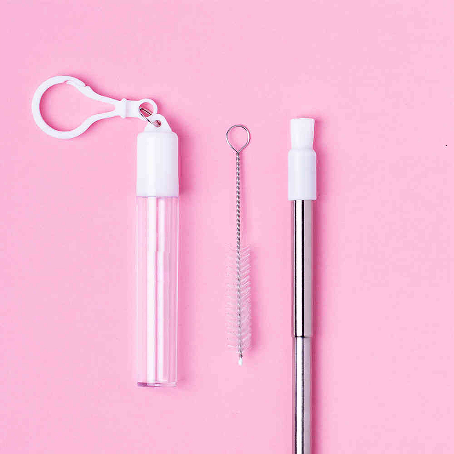 Una cannuccia riutilizzabile con spazzolino e custodia su sfondo rosa.