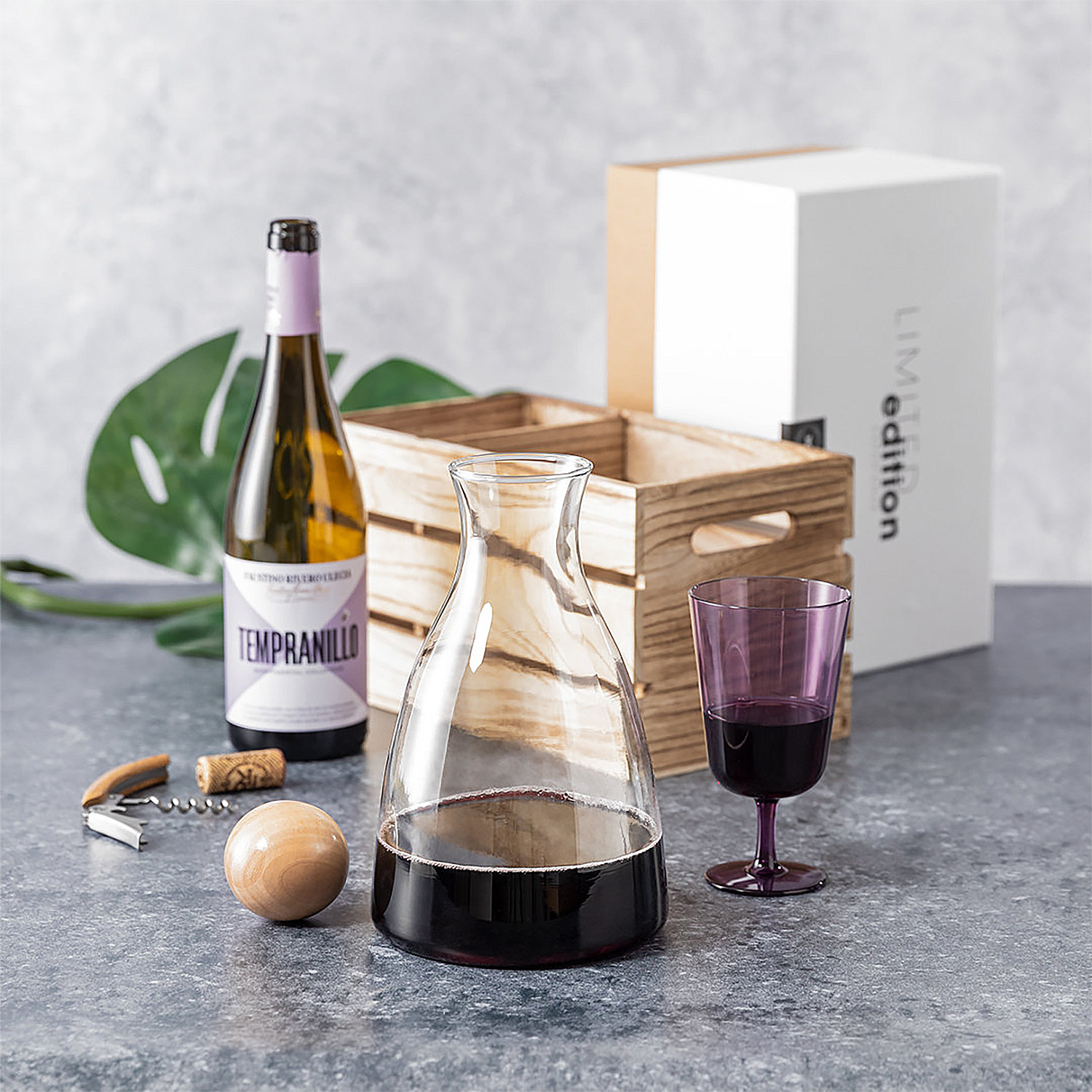Una botella de vino, decantador con vino, copa, sacacorchos y caja.