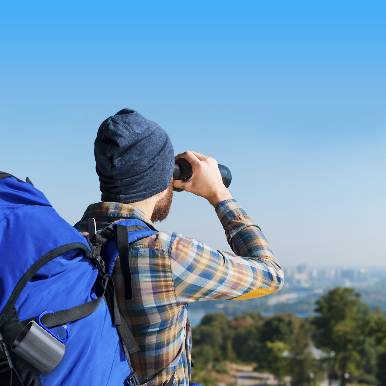 Uomo con berretto blu e camicia a quadri con zaino guarda la città con binocolo.