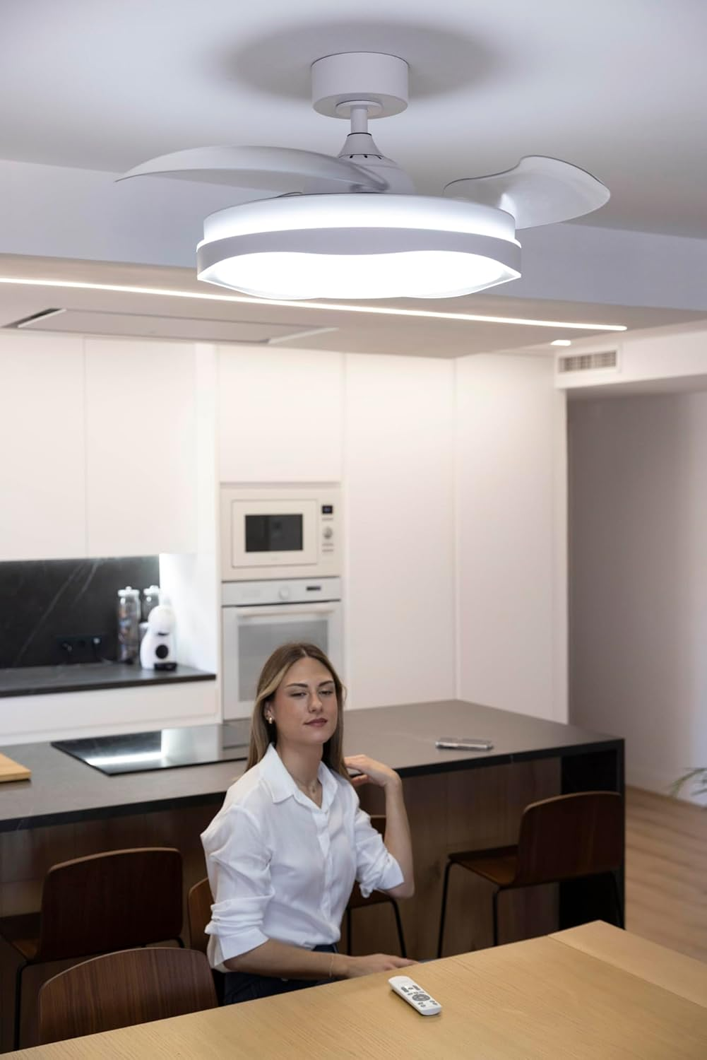 Una mujer se sienta a una mesa en una cocina moderna con ventilador de techo.