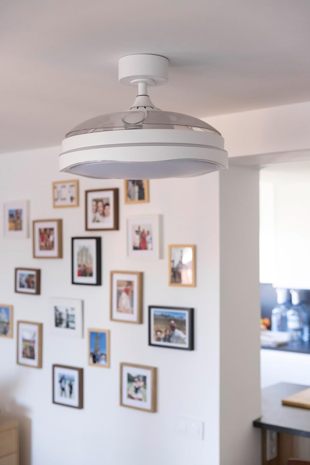 Una luz de techo blanca con ventilador sobre una pared llena de fotos enmarcadas.