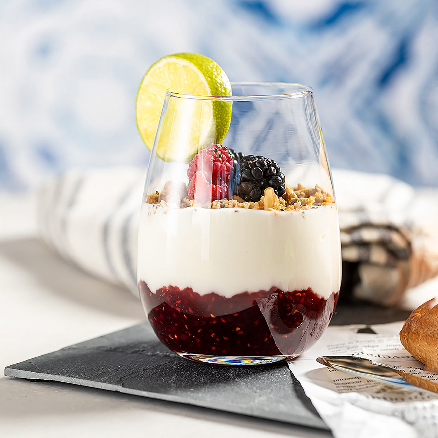 Un bicchiere con yogurt, frutti di bosco e marmellata, guarnito con lime.