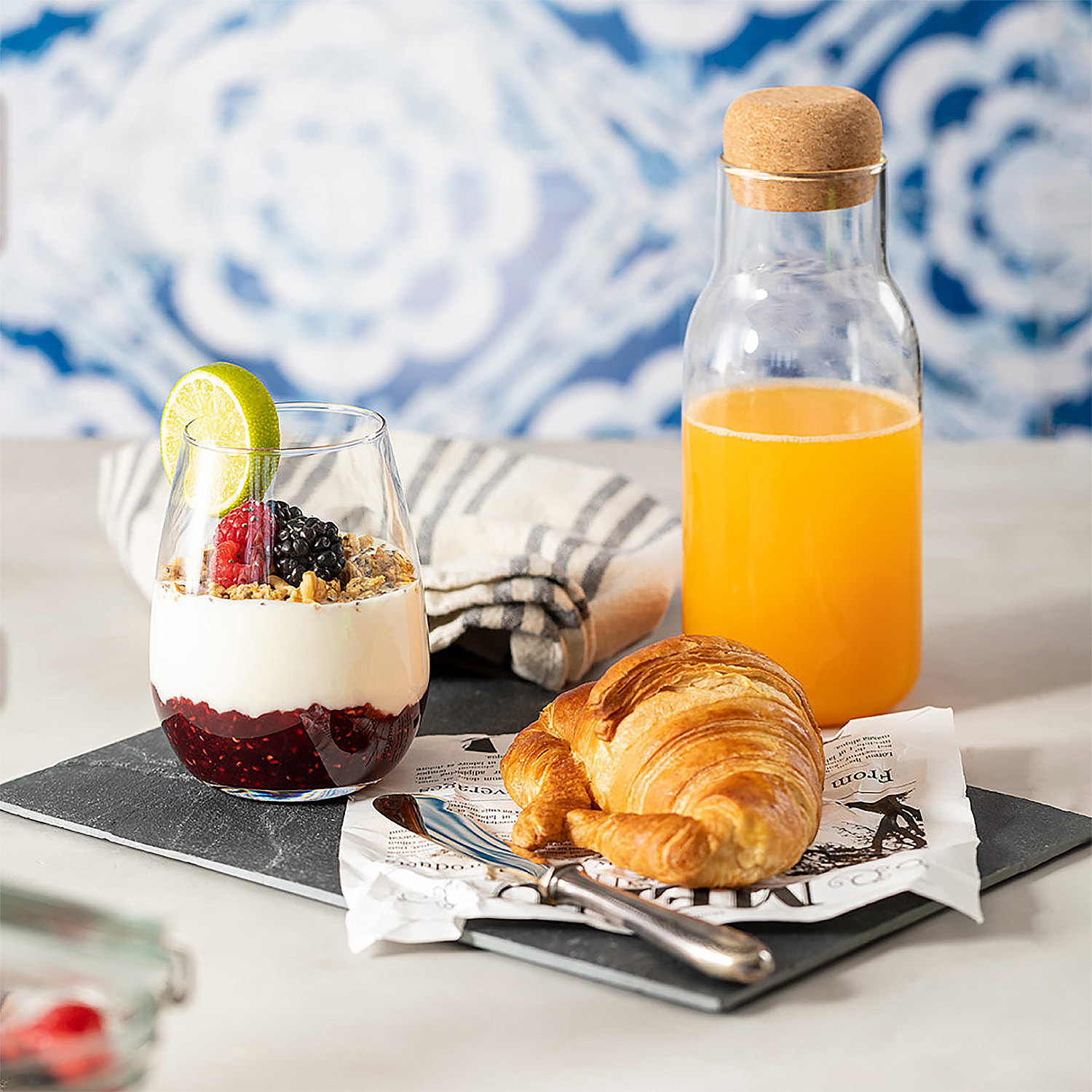 Un bicchiere di parfait di yogurt con frutti di bosco, croissant e succo d'arancia.