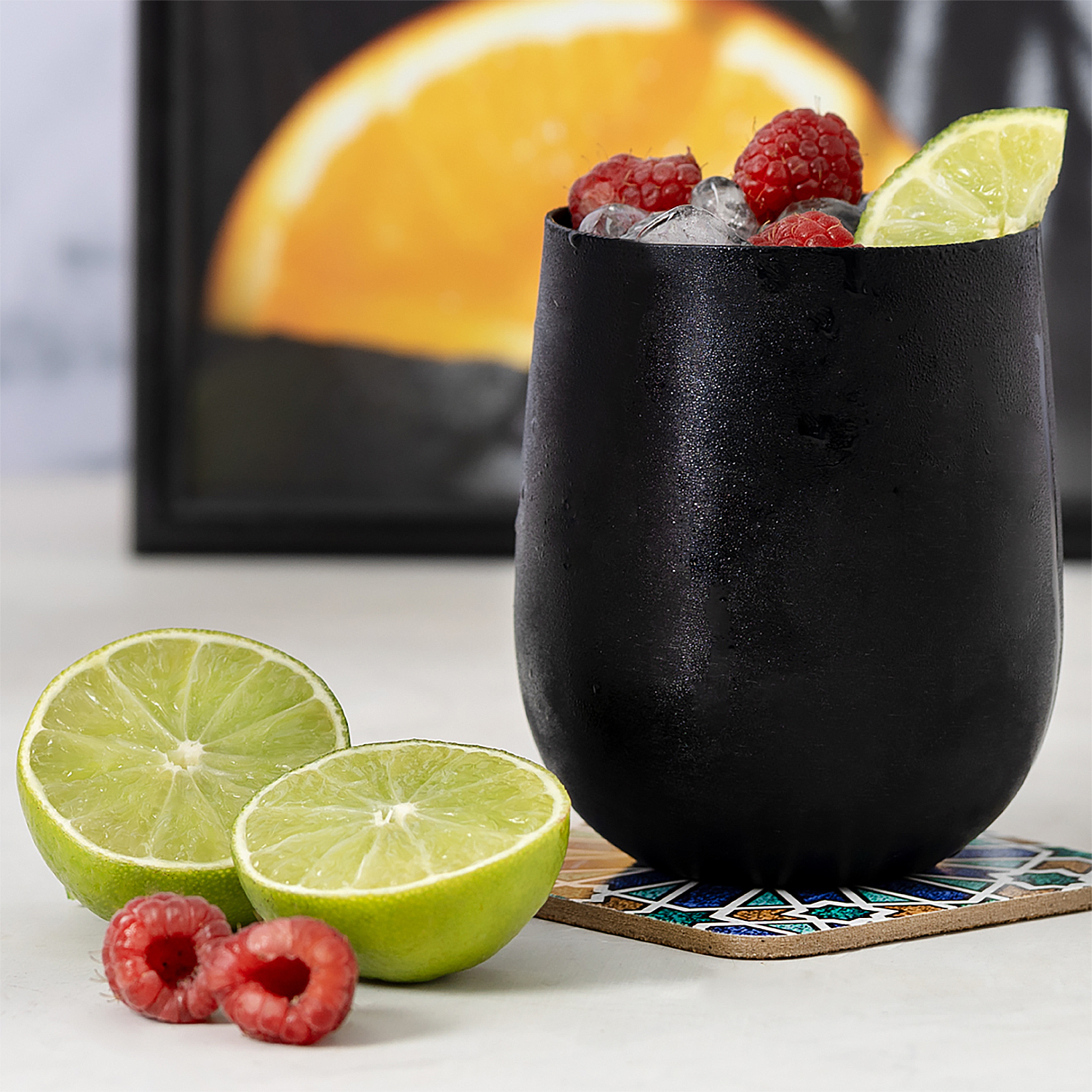 Una tazza nera con ghiaccio, bacche e lime. A sinistra ci sono due fette di lime e bacche.