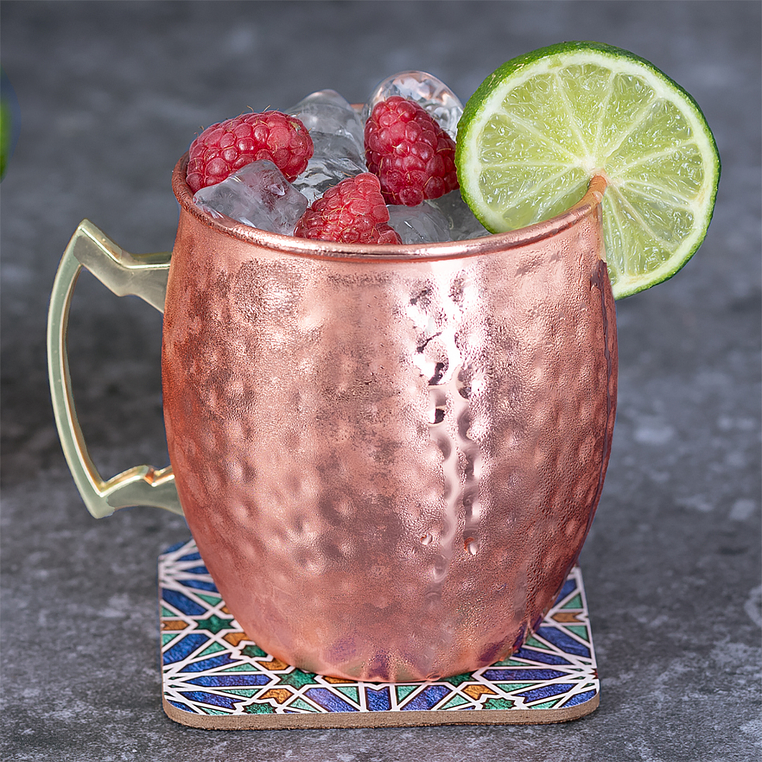 Una tazza di rame con ghiaccio, lamponi e una fetta di lime.