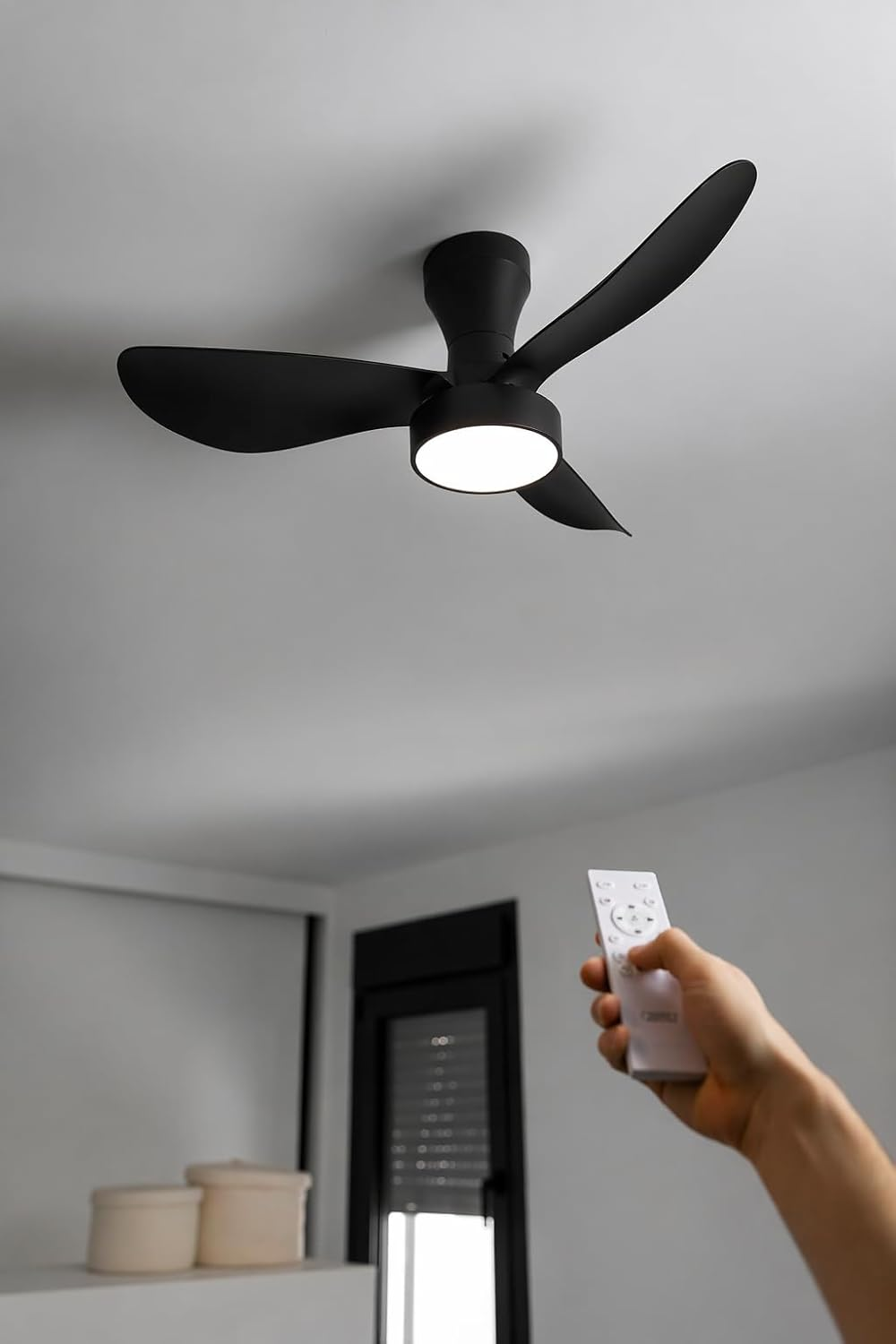Ventilador de techo negro con luz y una mano sosteniendo un mando a distancia.